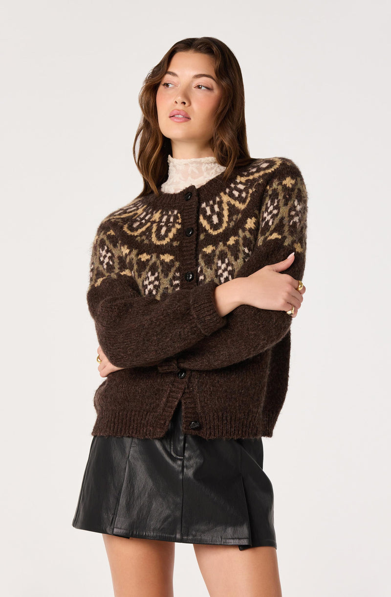 Woman wearing a patterned brown and beige knitted sweater over a white lace turtleneck, paired with a black leather skirt.