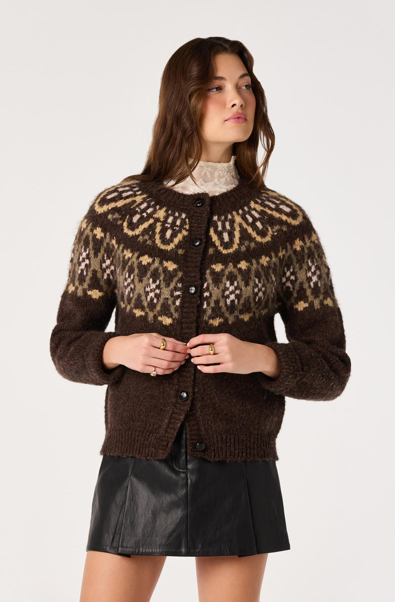 Woman wearing a brown patterned knit cardigan over a white lace turtleneck, paired with a black leather skirt.