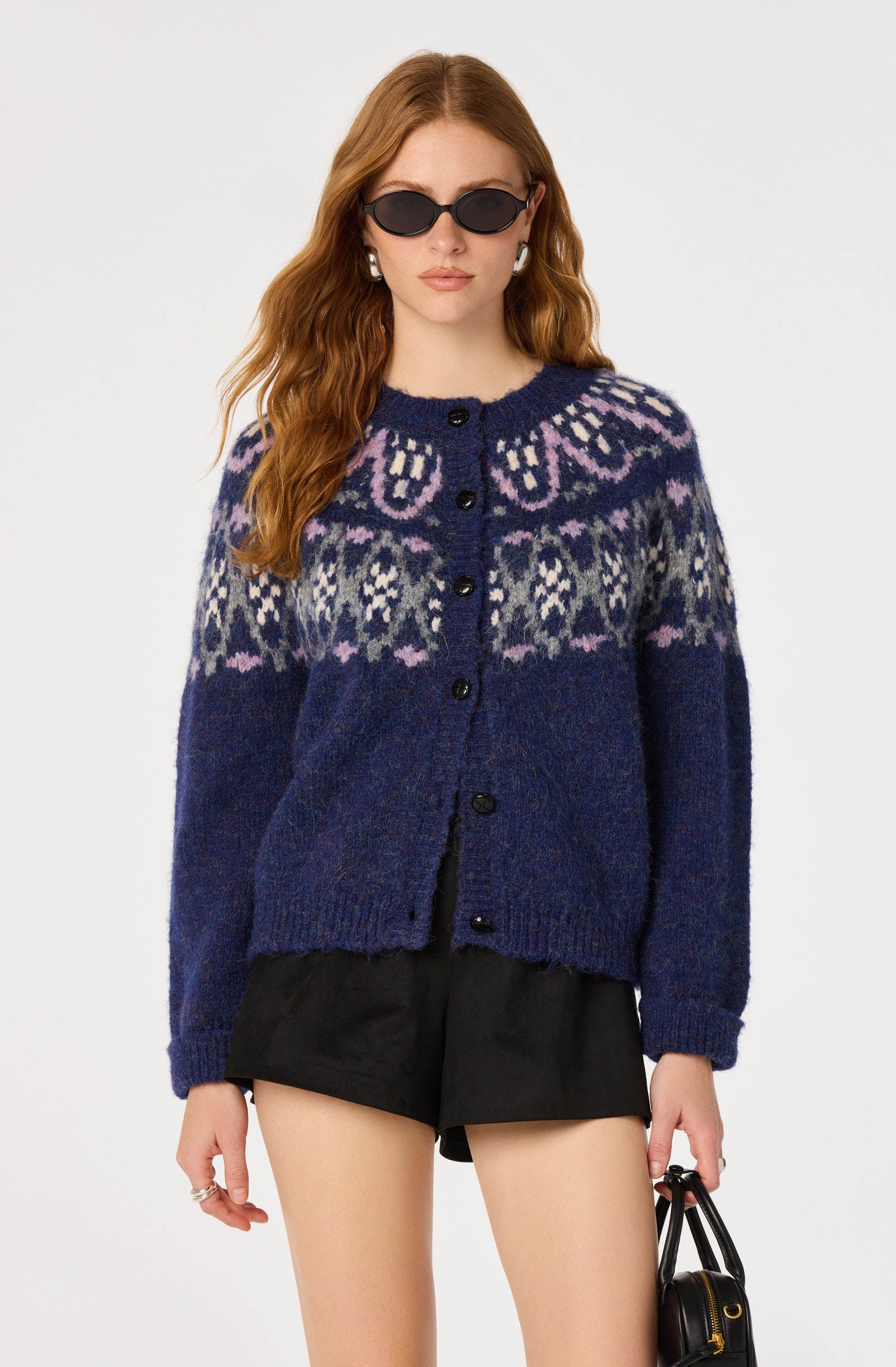 Woman wearing a dark blue patterned knit cardigan, black shorts, and sunglasses.