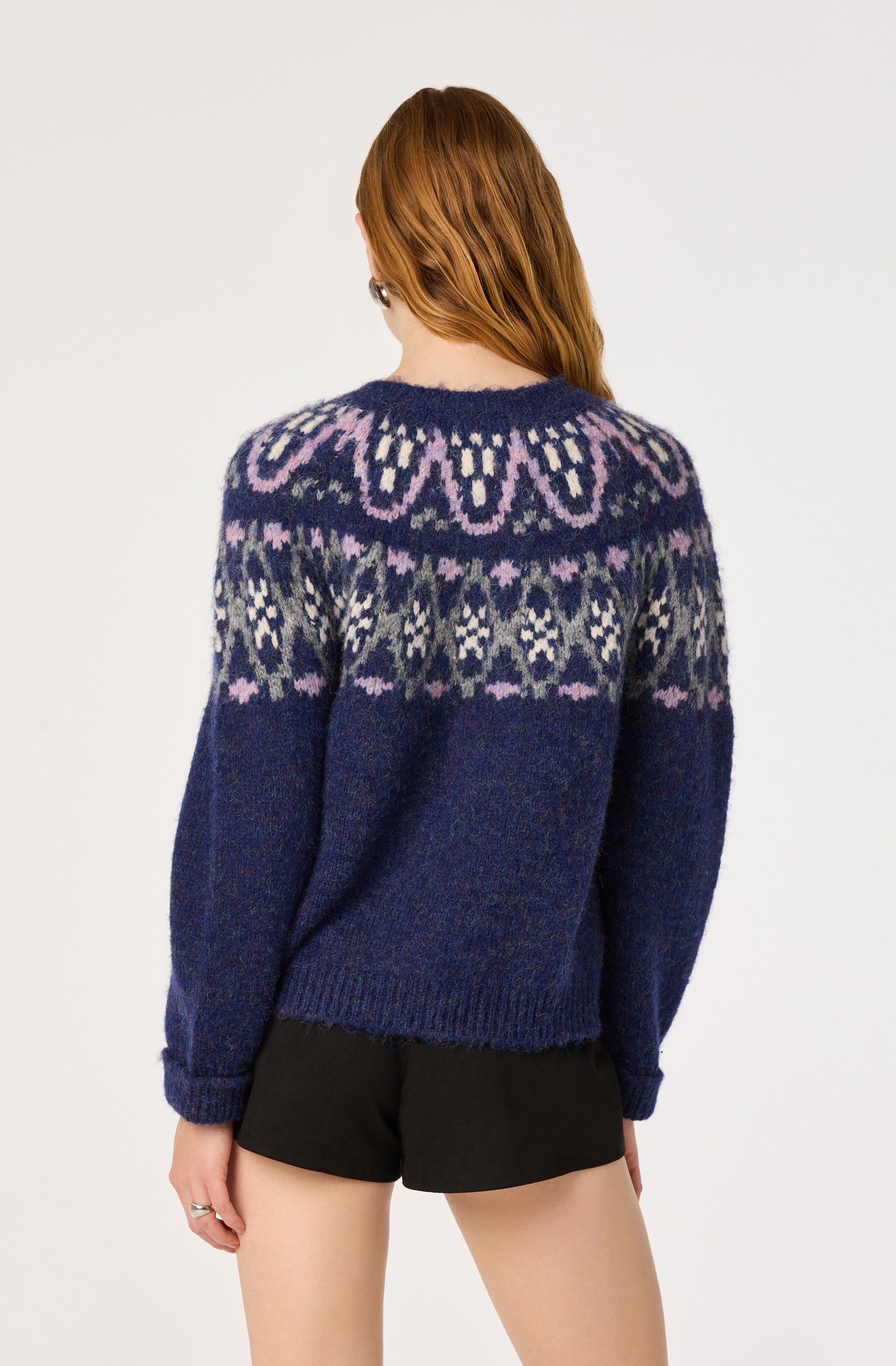 Woman wearing a navy blue sweater with purple, white, and gray Nordic pattern, paired with black shorts.