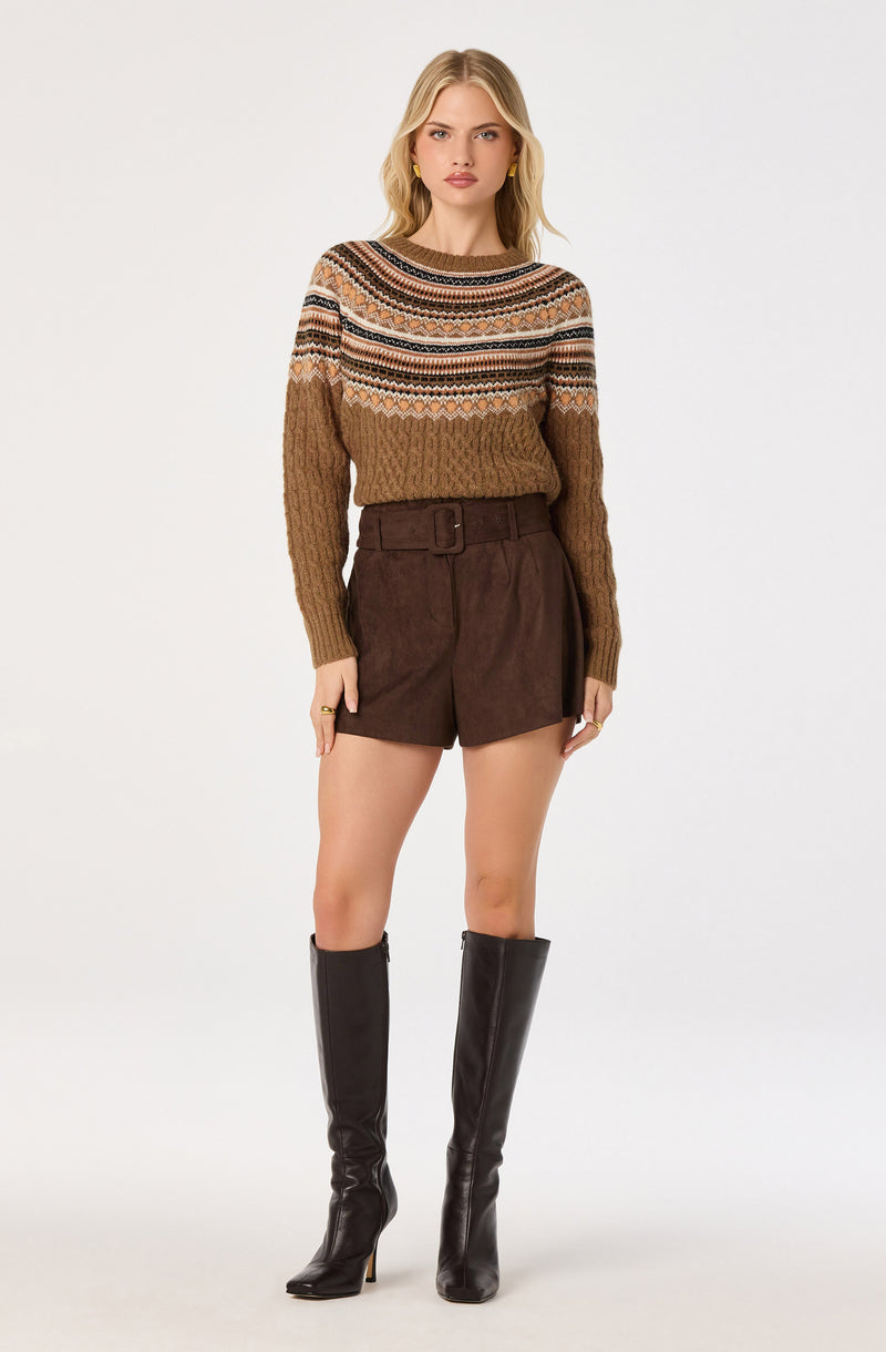 Woman wearing a patterned knit sweater, brown shorts with a belt, and tall black boots.