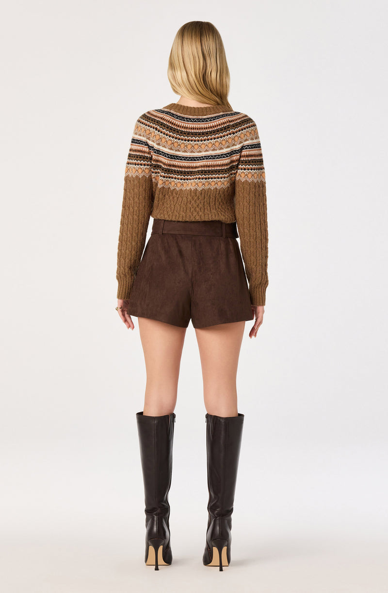 Woman wearing a patterned knit sweater, brown shorts, and tall black boots.