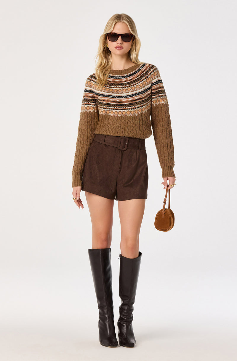 Woman wearing a multicolored striped sweater, brown high-waisted shorts, and knee-high black boots, holding a small brown purse.