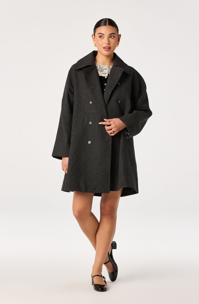 Woman wearing a dark gray double-breasted coat with wide lapel and black shoes.