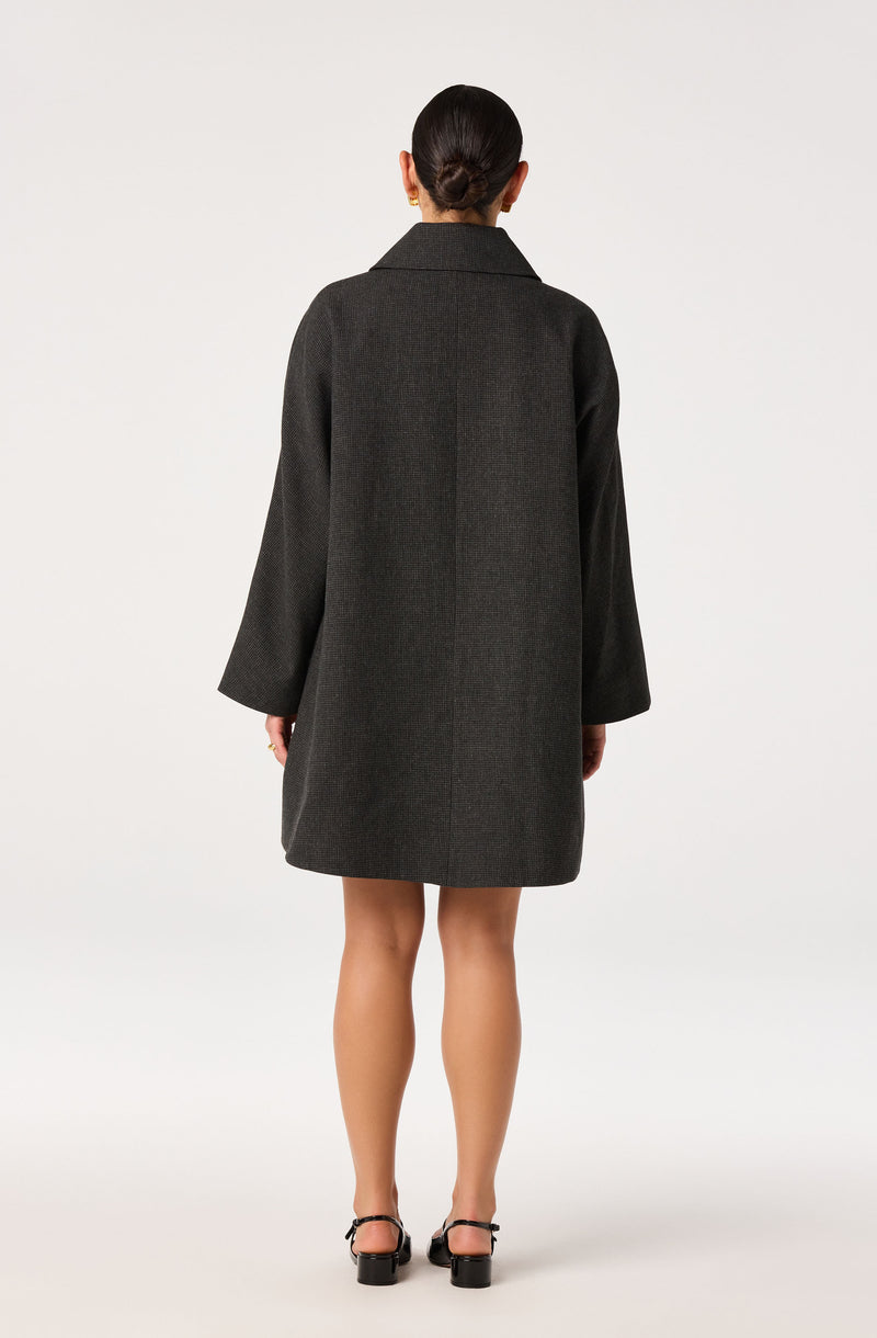 Woman wearing a dark gray oversized coat with long sleeves and black heeled sandals.