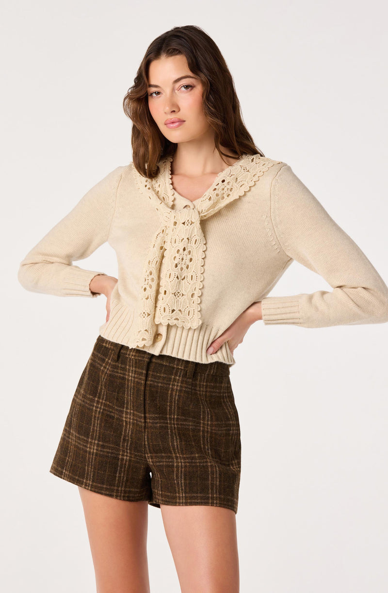 Cream sweater with lace collar and dark plaid shorts.