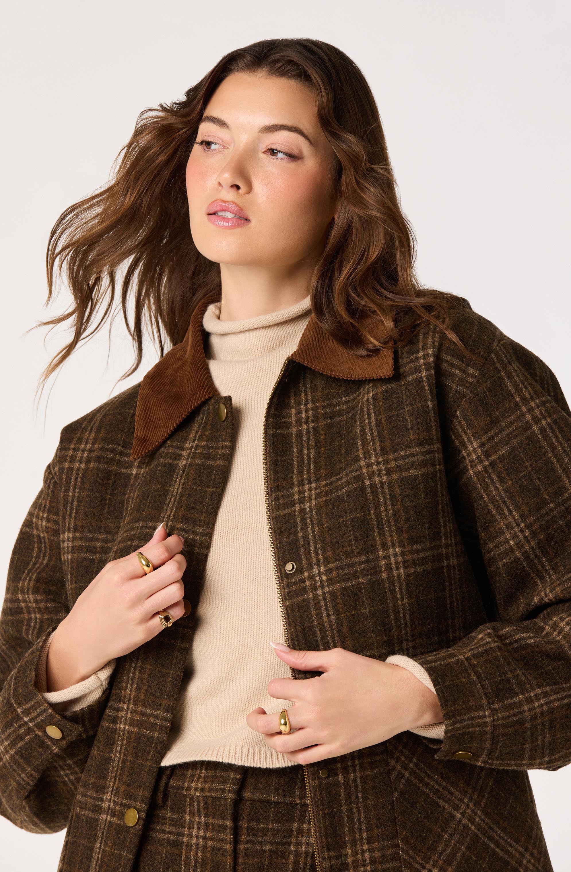 Woman wearing a brown plaid jacket with a tan collar over a beige turtleneck sweater.
