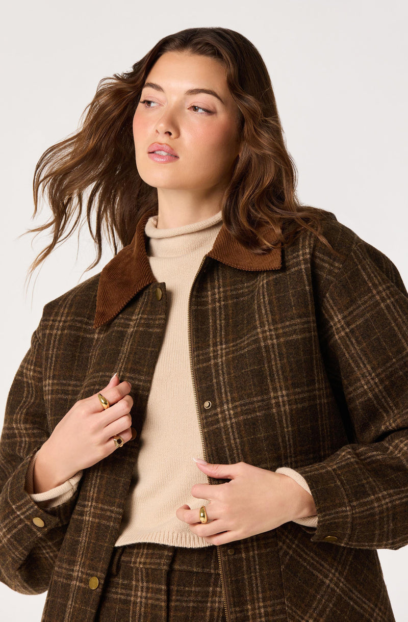 Woman wearing a brown plaid jacket with a tan collar over a beige turtleneck sweater.