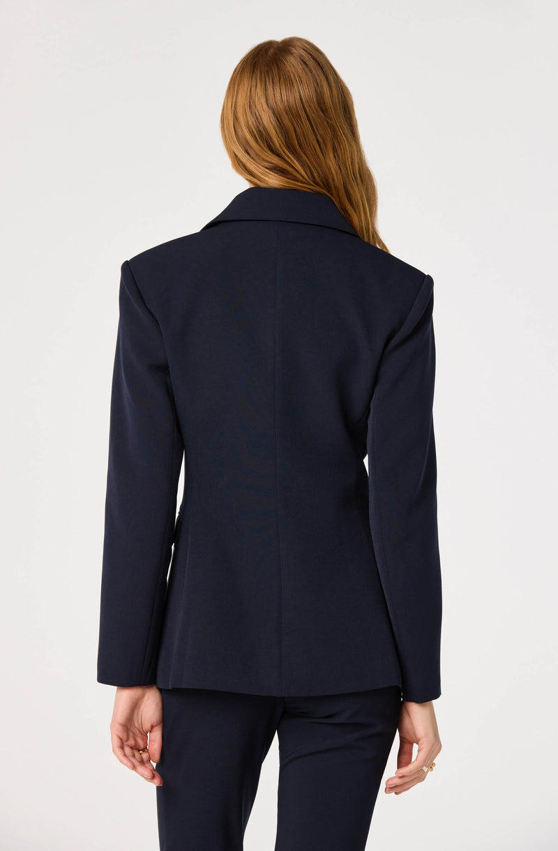 Woman in a navy blazer and matching navy pants, with red hair.