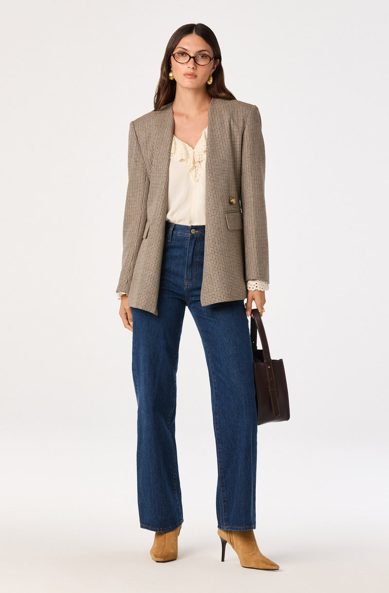 Women wearing a plaid blazer, cream blouse, blue jeans, tan high heels, and holding a dark handbag.