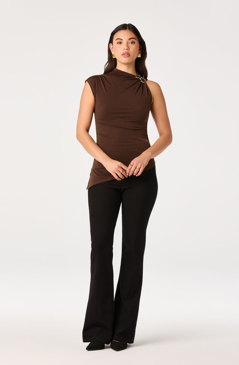 Woman wearing a sleeveless brown top with a knot detail and black flared pants.
