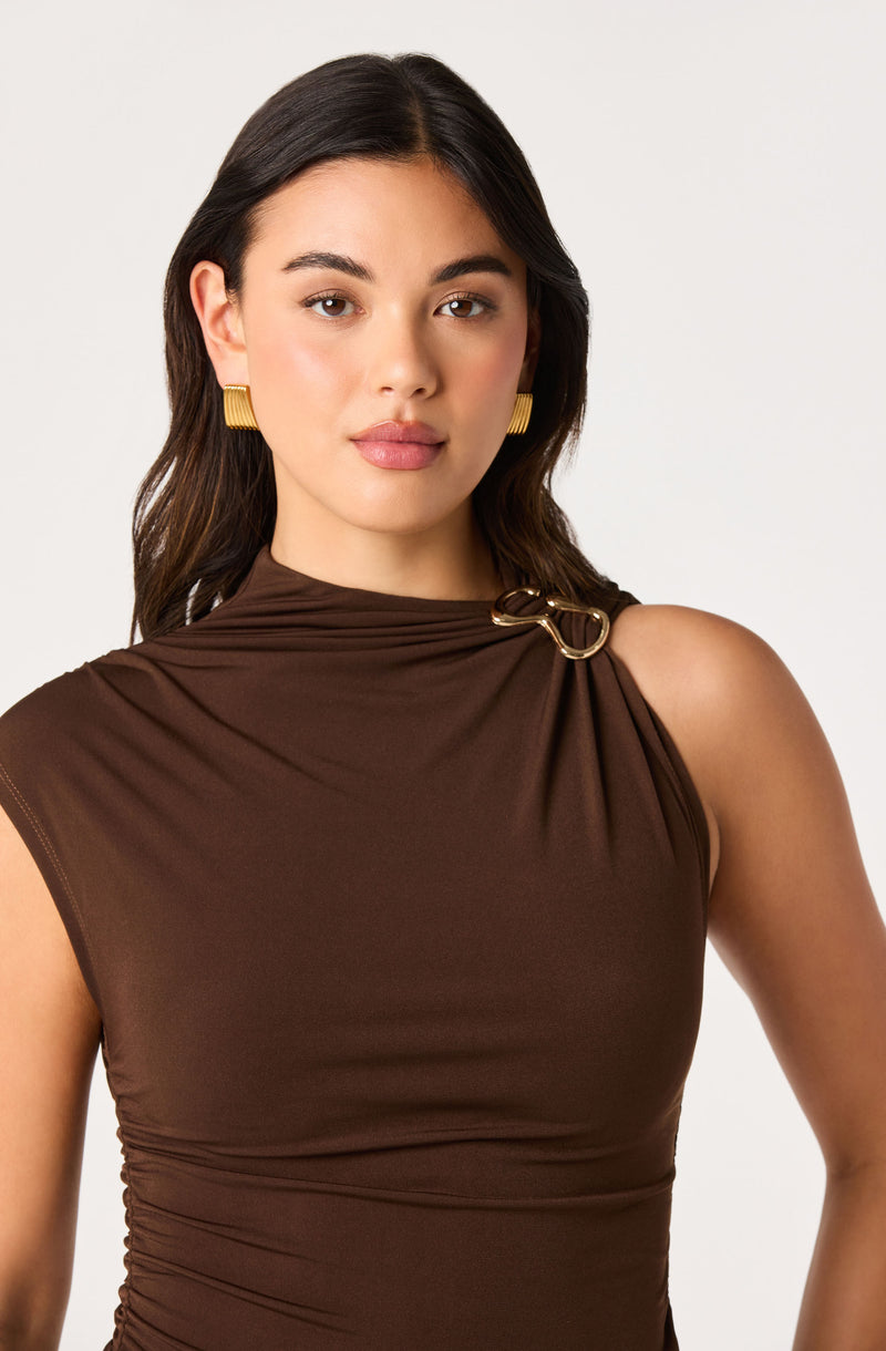 Woman wearing a sleeveless brown top with a gold ring detail at the shoulder.