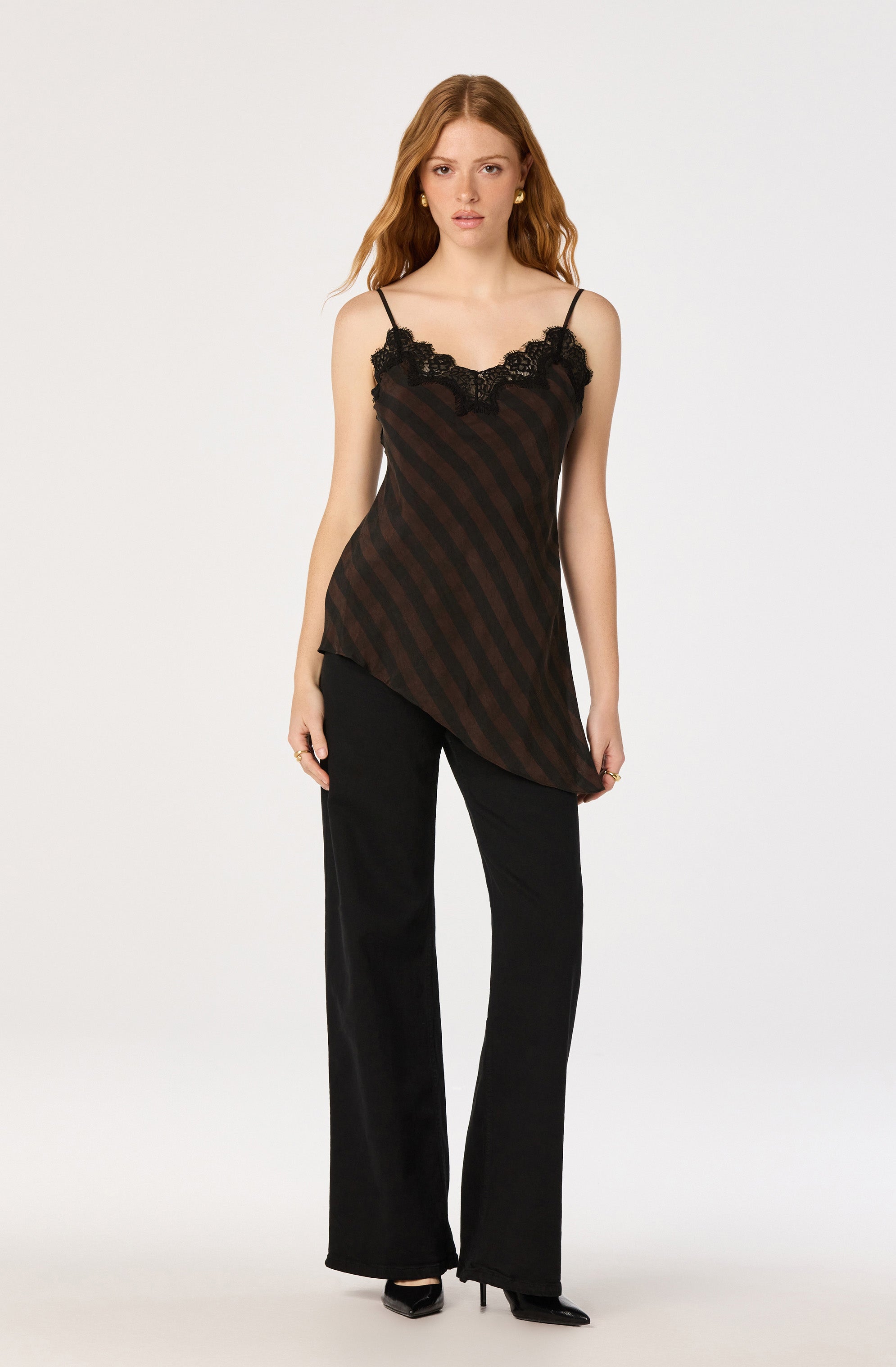 Woman wearing a black and brown striped slip top with lace detail, paired with black wide-leg pants and black heels.