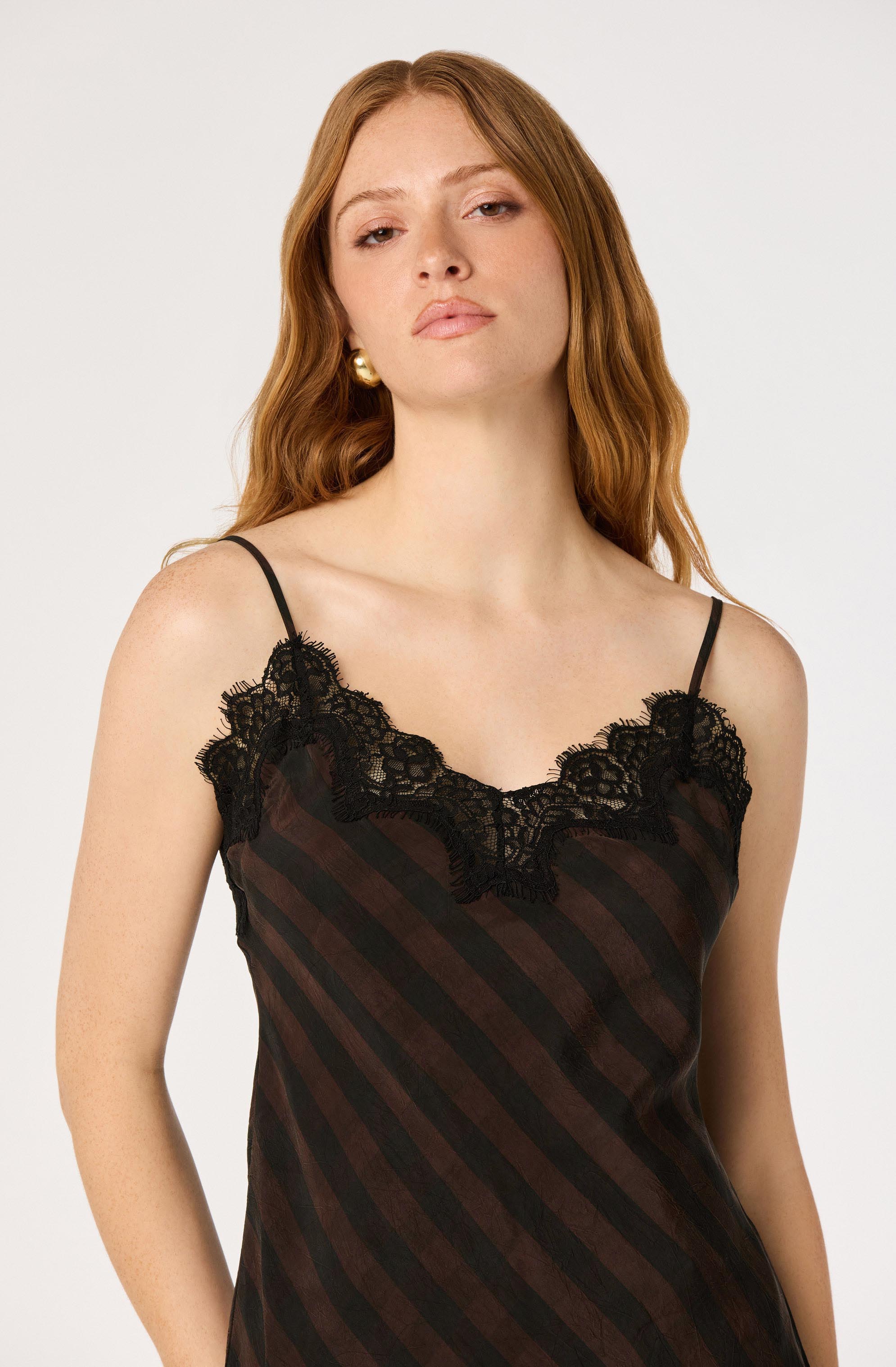 Woman wearing a black and red striped satin slip dress with black lace trim and spaghetti straps.