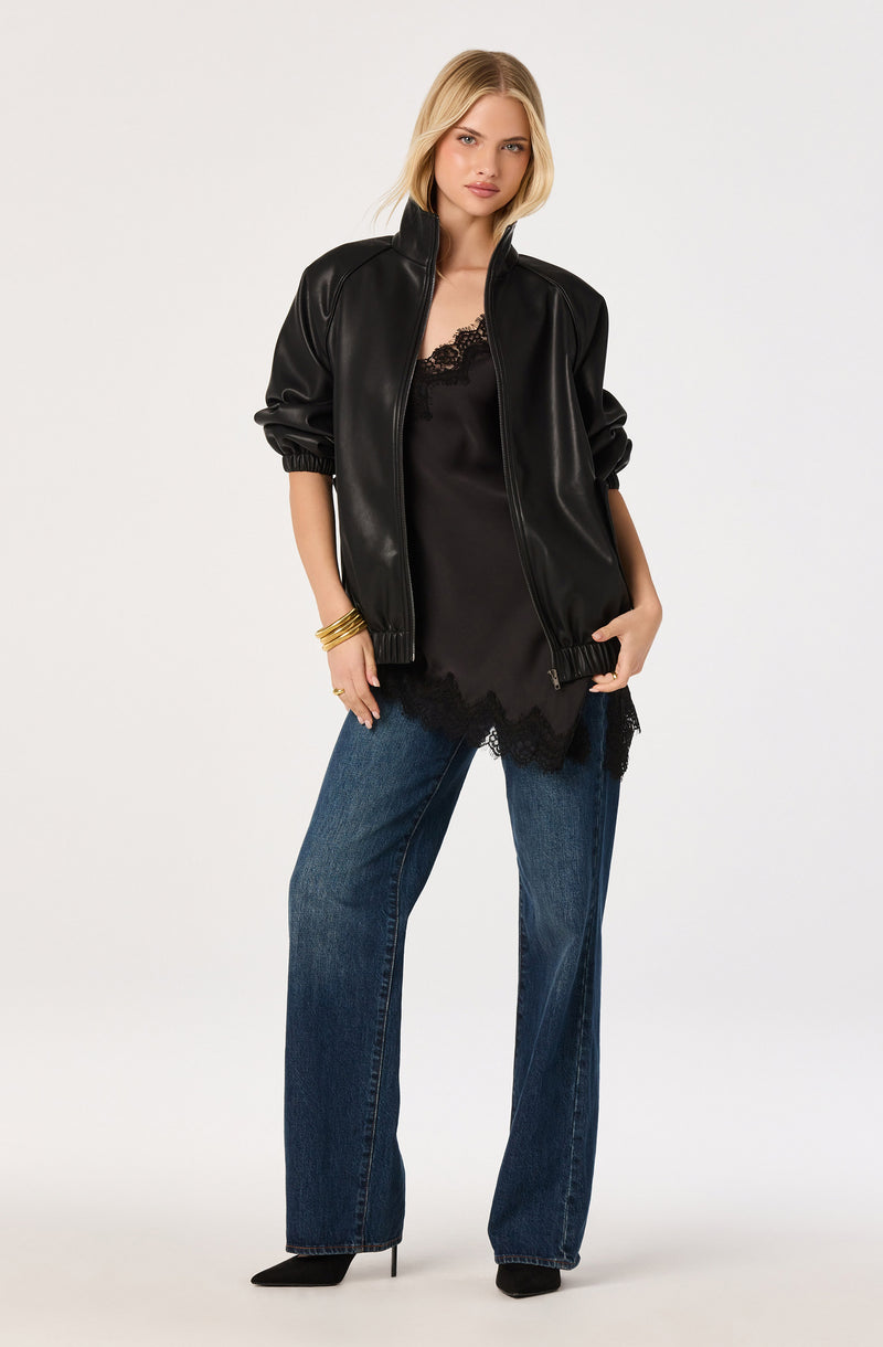 Woman wearing a black leather jacket, black lace-trim camisole, blue jeans, and black heels.