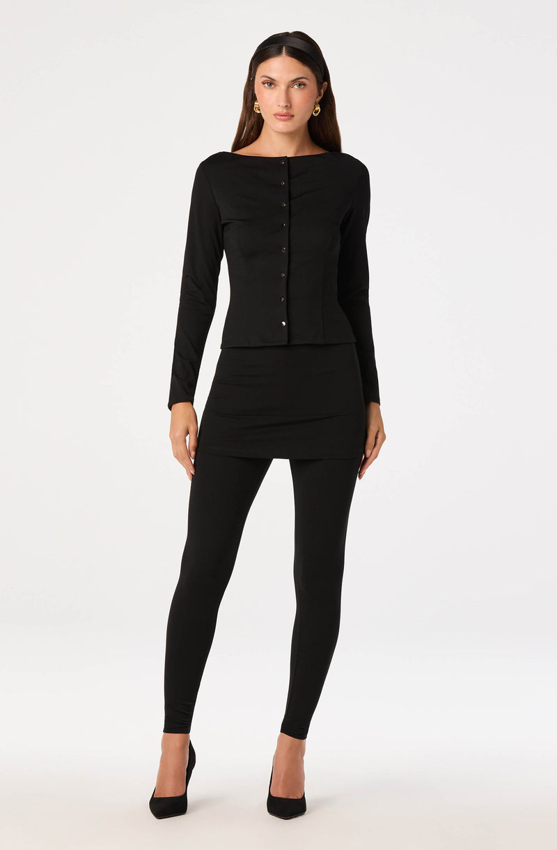 Woman wearing a black long-sleeve button-up top, black mini skirt, black leggings, and black high heels.
