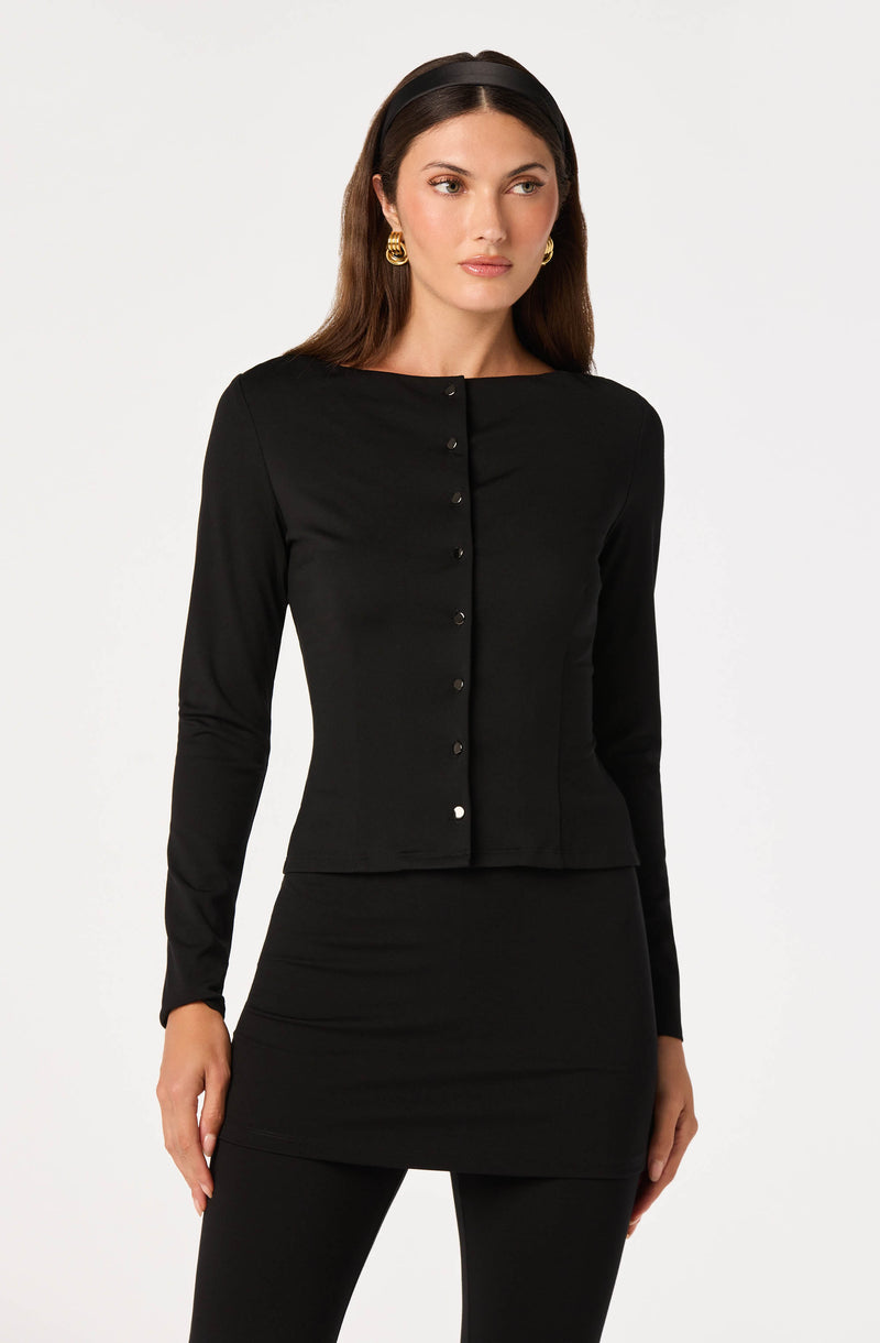 Woman in black long-sleeve top and black skirt or pants, gold earrings, black headband.