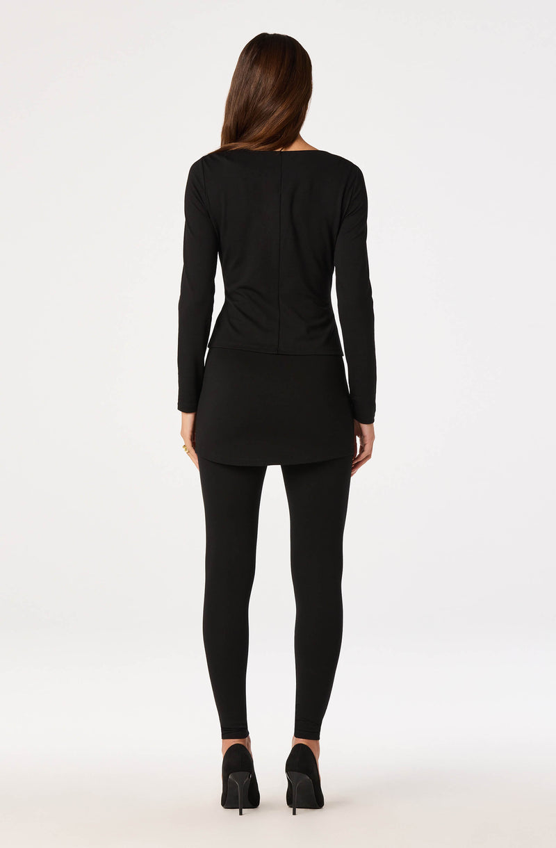 Woman in black long-sleeve top, fitted skirt, and black leggings, wearing high heels.