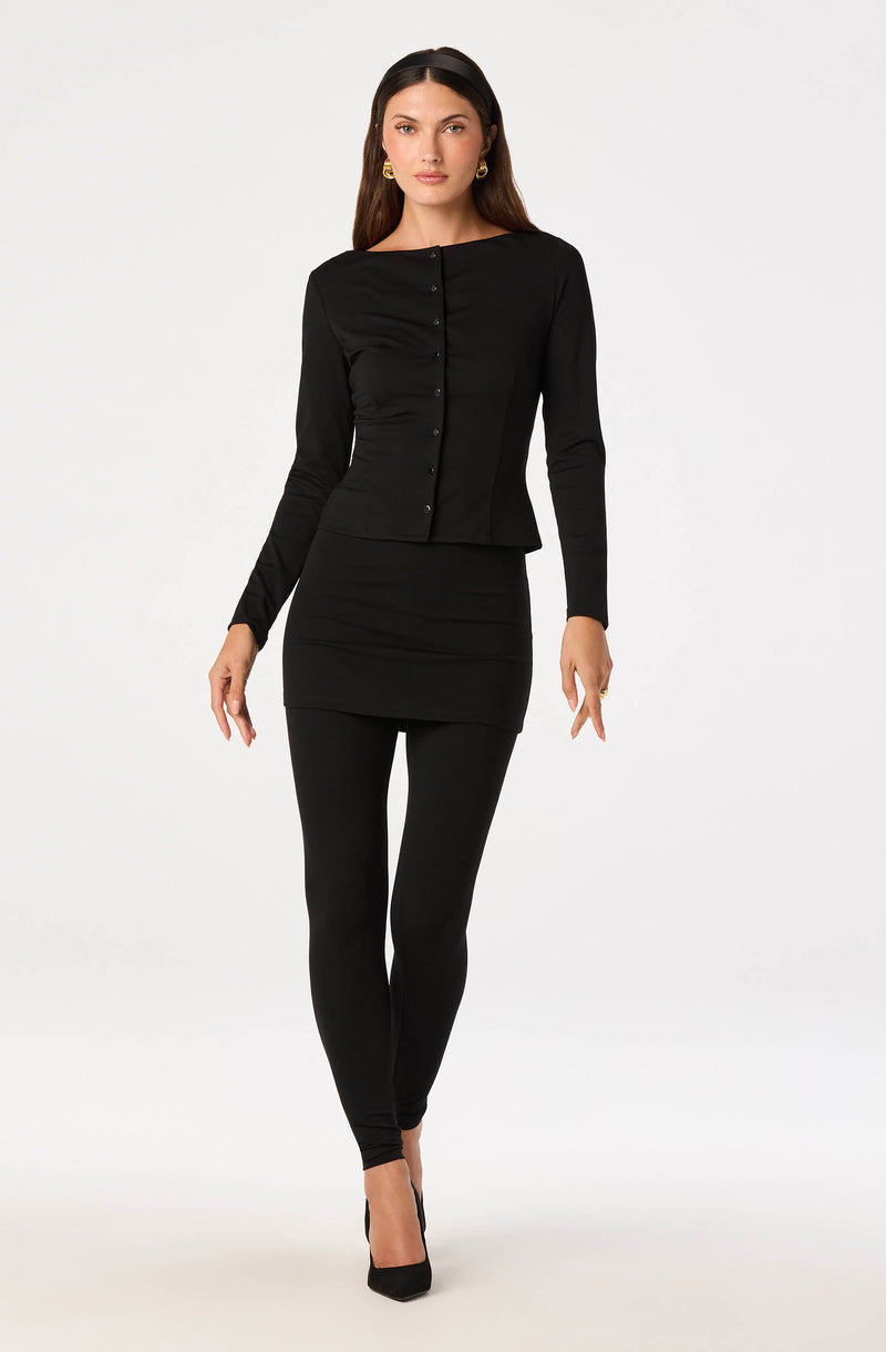 Woman in black long-sleeve top with buttons and matching black leggings, black heels.