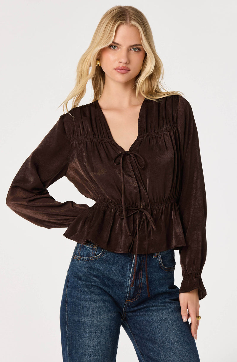 Brown long-sleeve blouse with a tie-front and ruched details, paired with blue jeans.