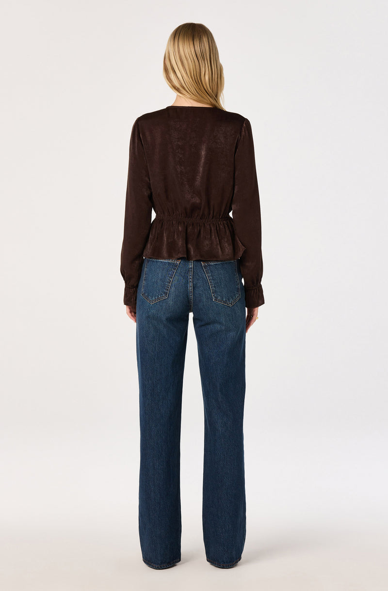 Woman wearing a dark brown long-sleeve top with elastic waist and blue wide-leg jeans.