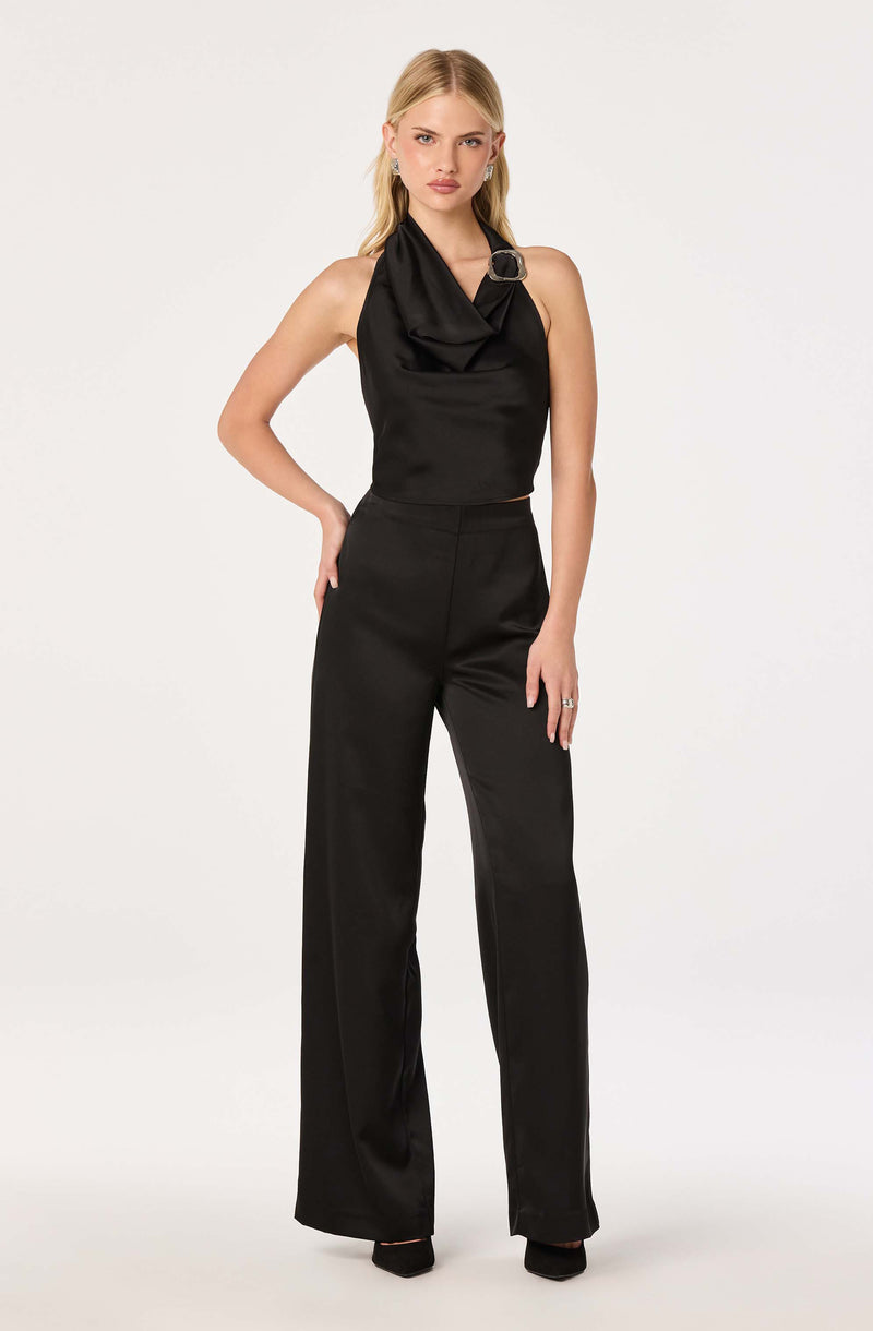 Woman in black sleeveless top with a draped neckline and large buckle detail, paired with matching high-waisted wide-leg pants.