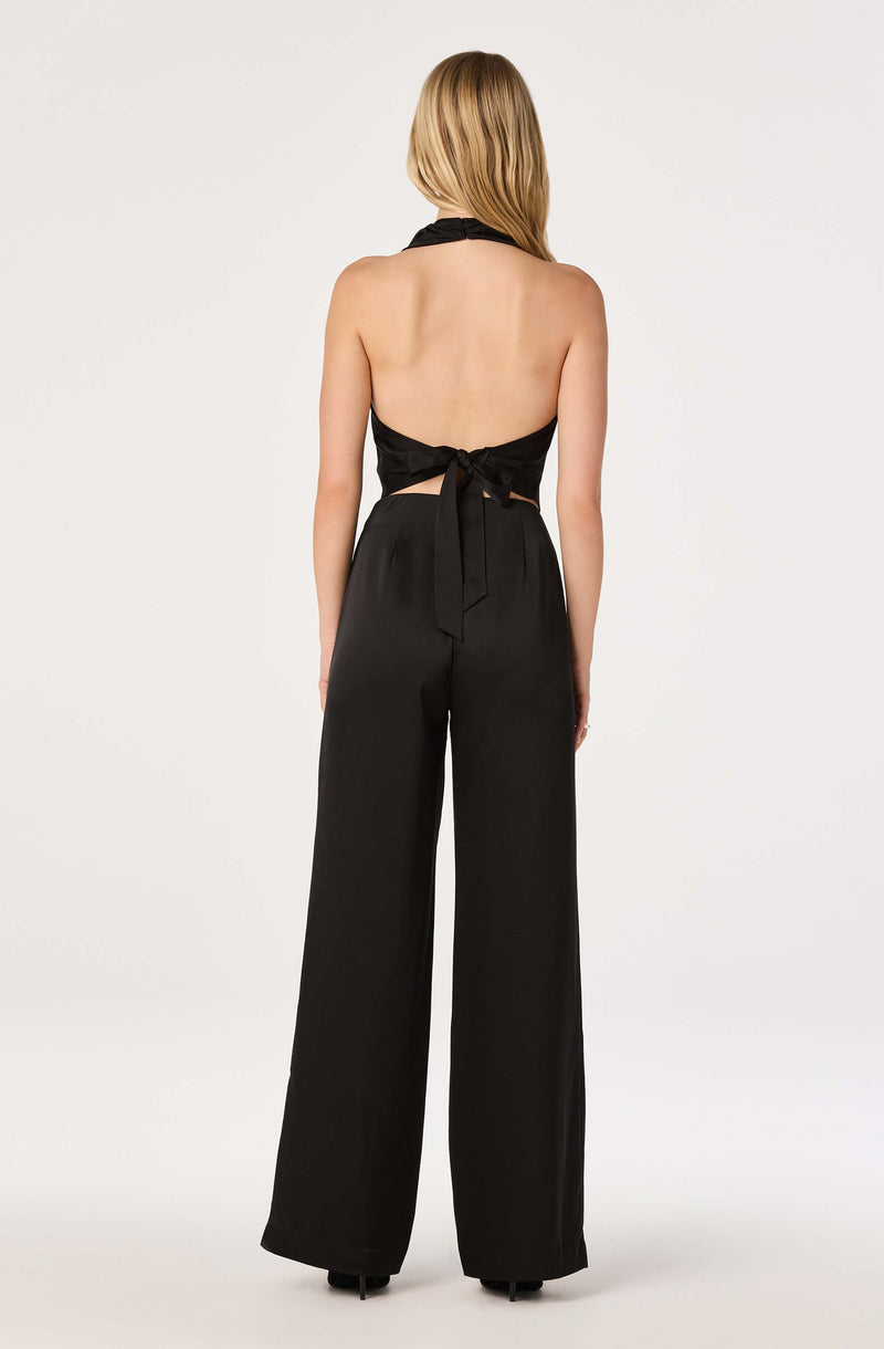 Back view of a woman wearing a black halter top with a bow and wide-legged black pants.