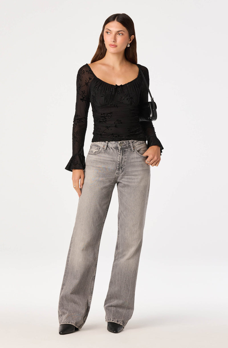 Woman wearing a black lace long-sleeve top and wide-leg gray jeans.