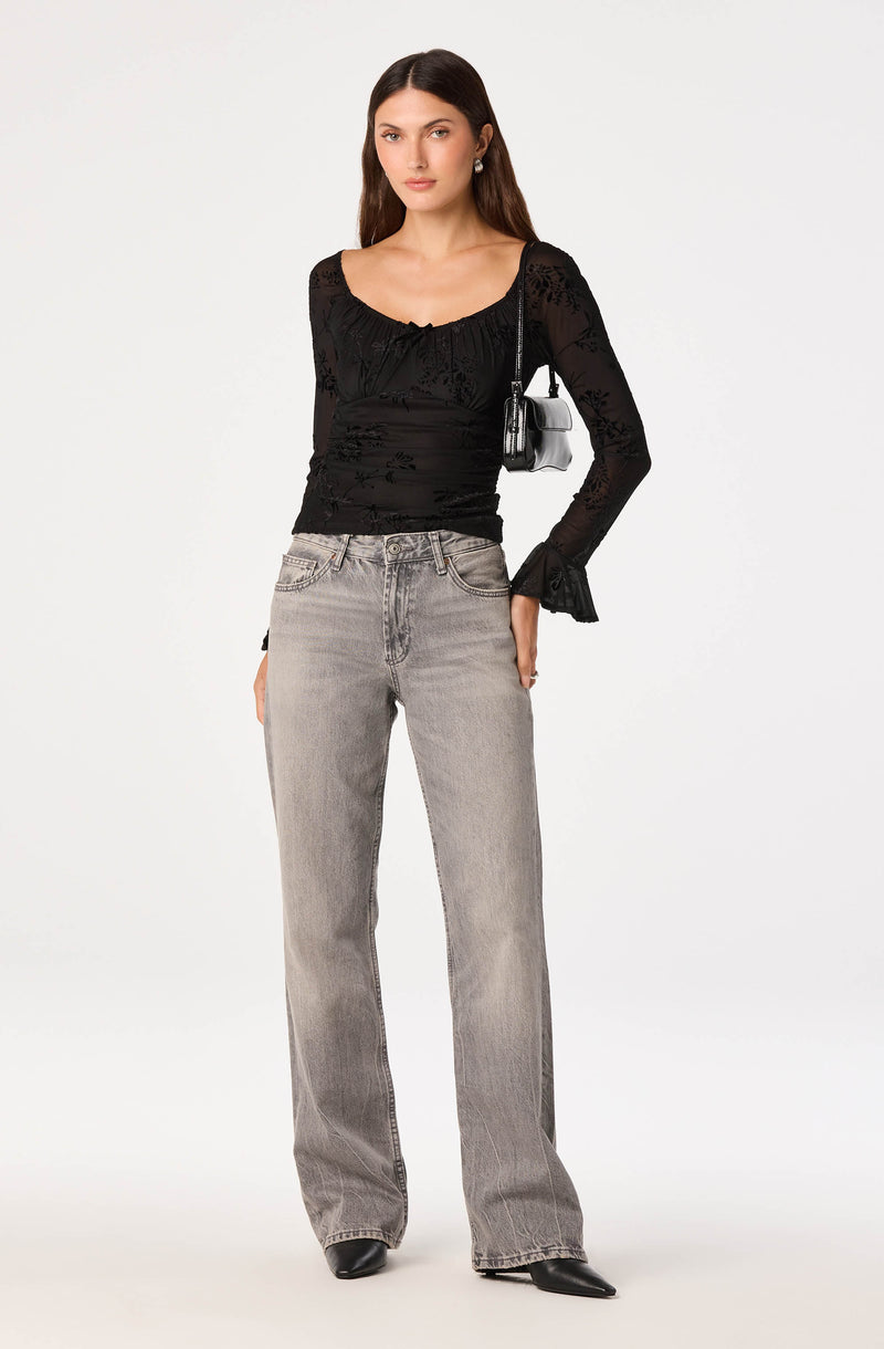 Woman wearing a black lace long-sleeve top, gray high-waisted jeans, and black shoes.