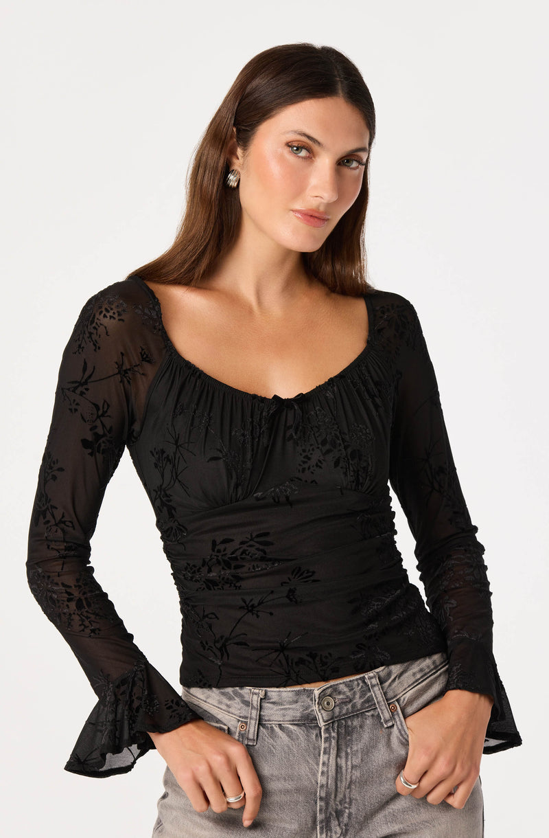 Woman wearing a black, floral-patterned, long-sleeve blouse with ruffled cuffs and a scoop neckline.