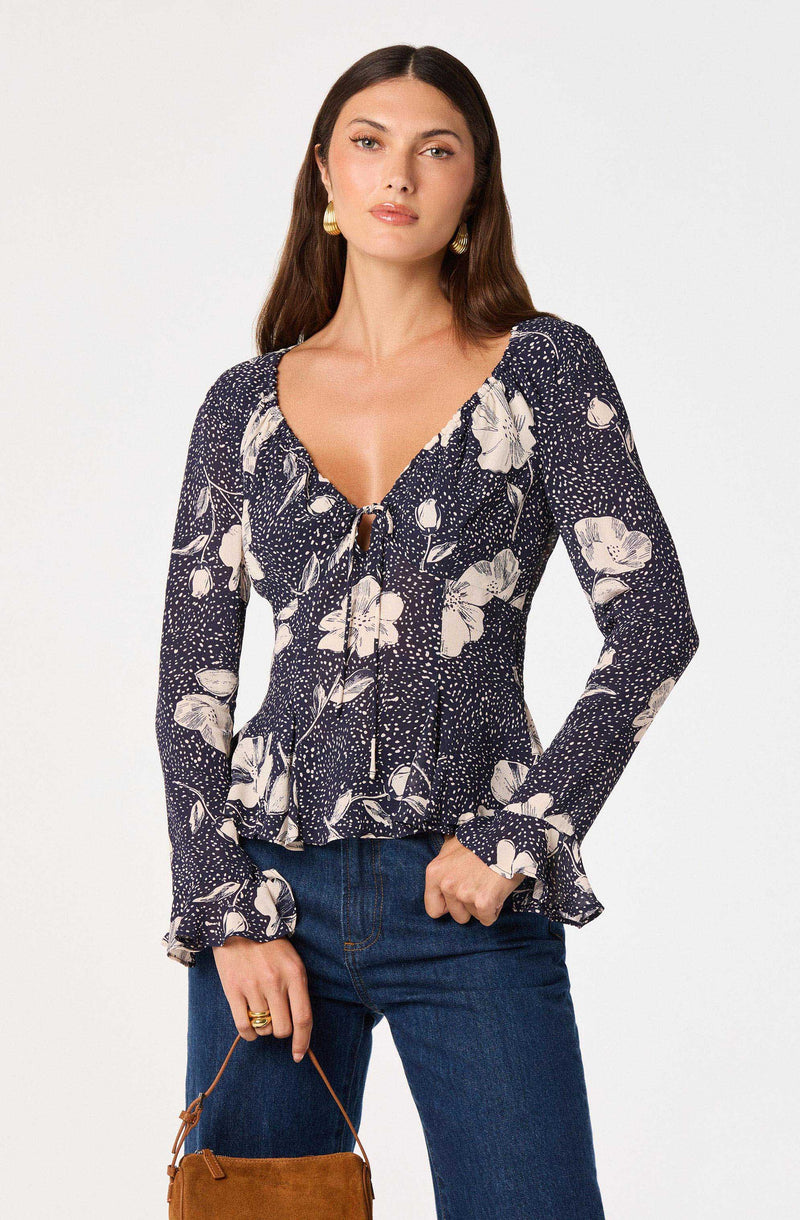 Woman wearing a navy floral print long-sleeve blouse with ruffled cuffs and neckline.