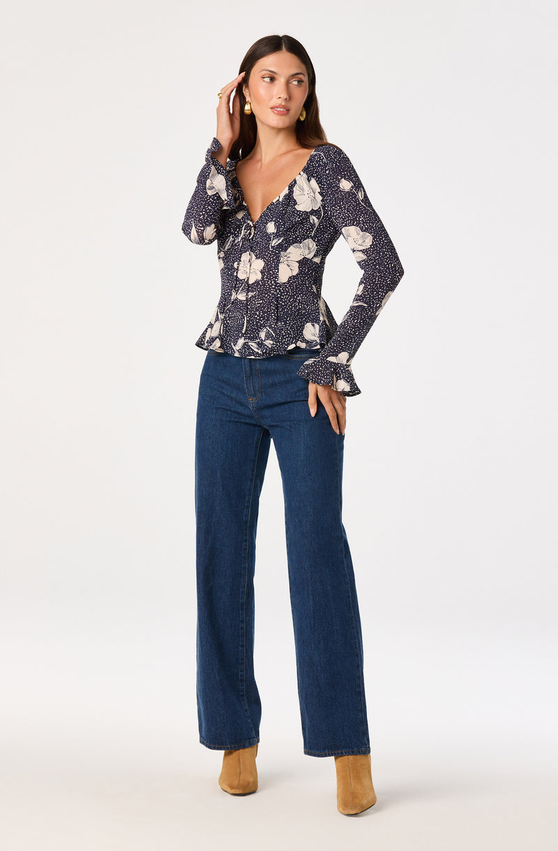 Woman wearing a navy floral blouse with ruffled cuffs and wide-leg jeans, beige boots.