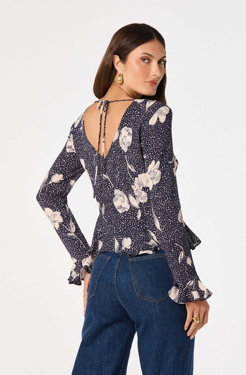Woman wearing a navy floral long-sleeve top with ruffled cuffs and a tie back.