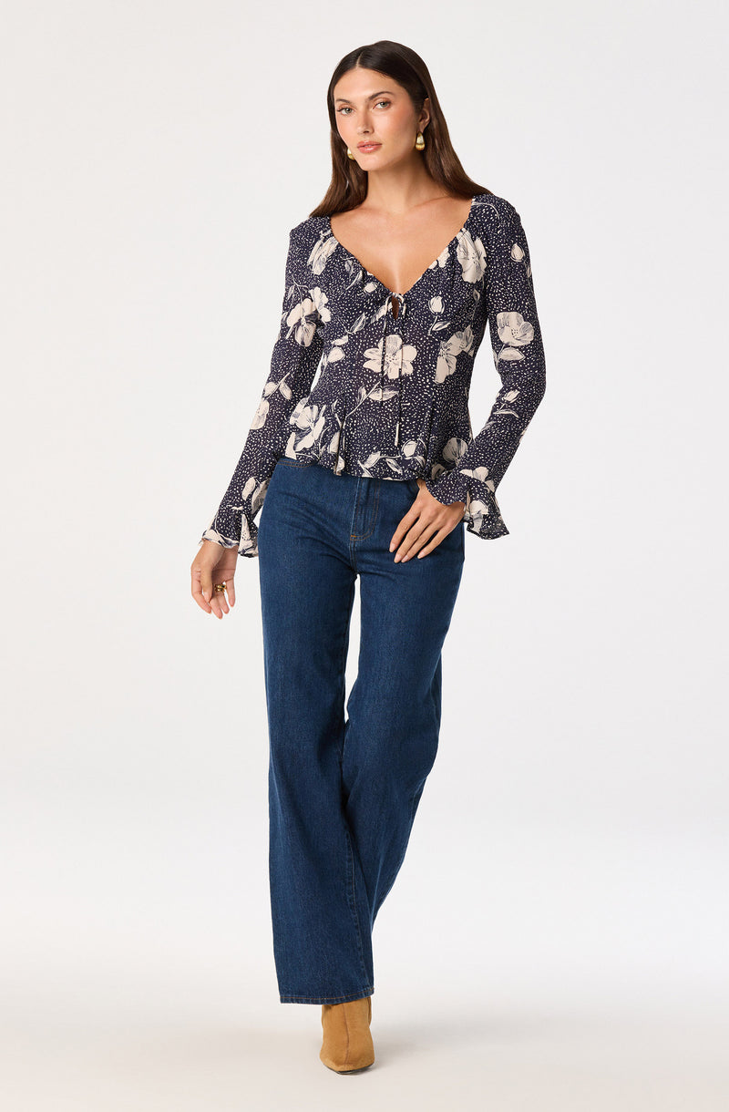 Woman wearing a long-sleeve floral blouse with ruffled cuffs and high-waisted blue jeans.