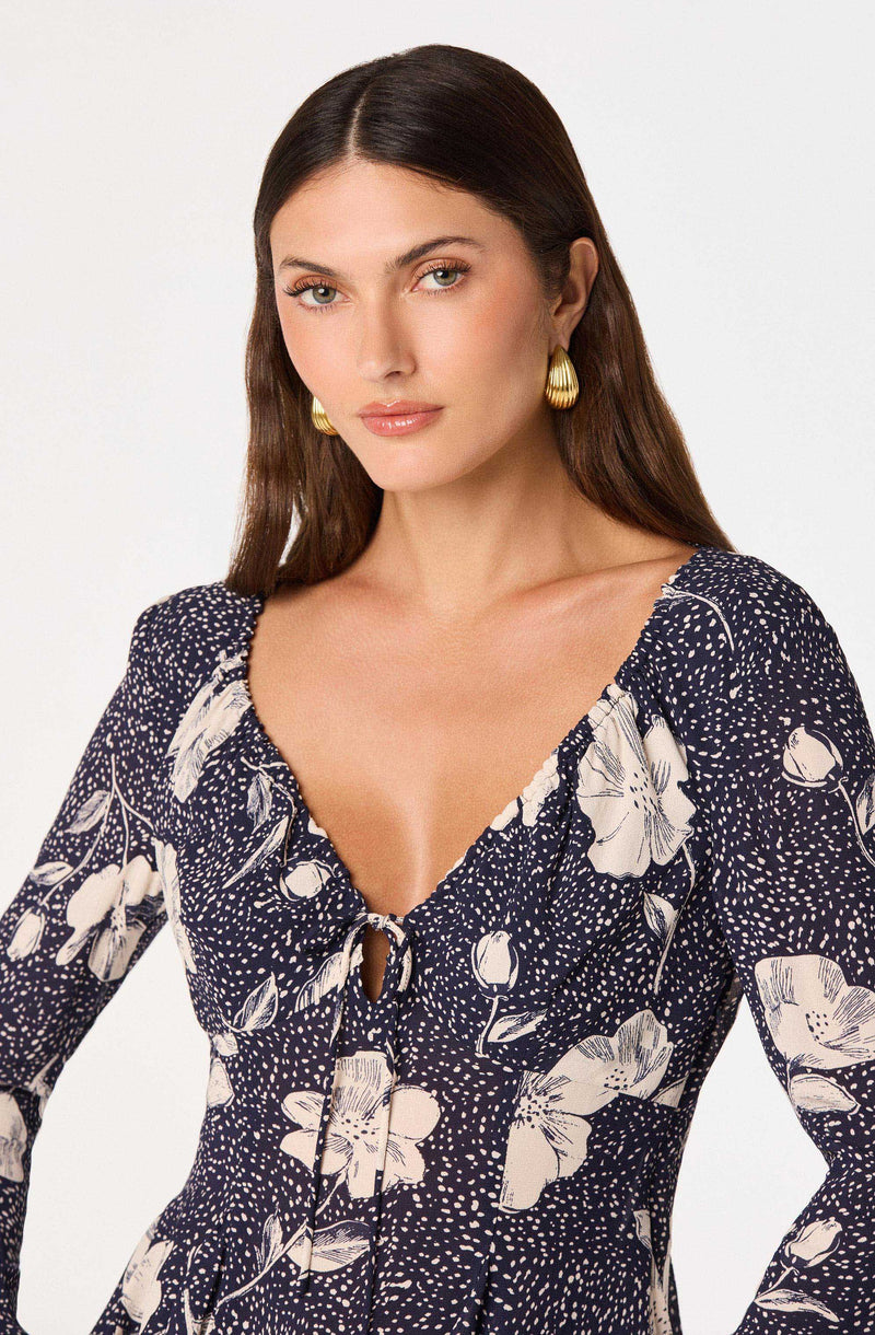 Woman wearing a dark blue dress with white floral patterns and a keyhole tie at the neckline.