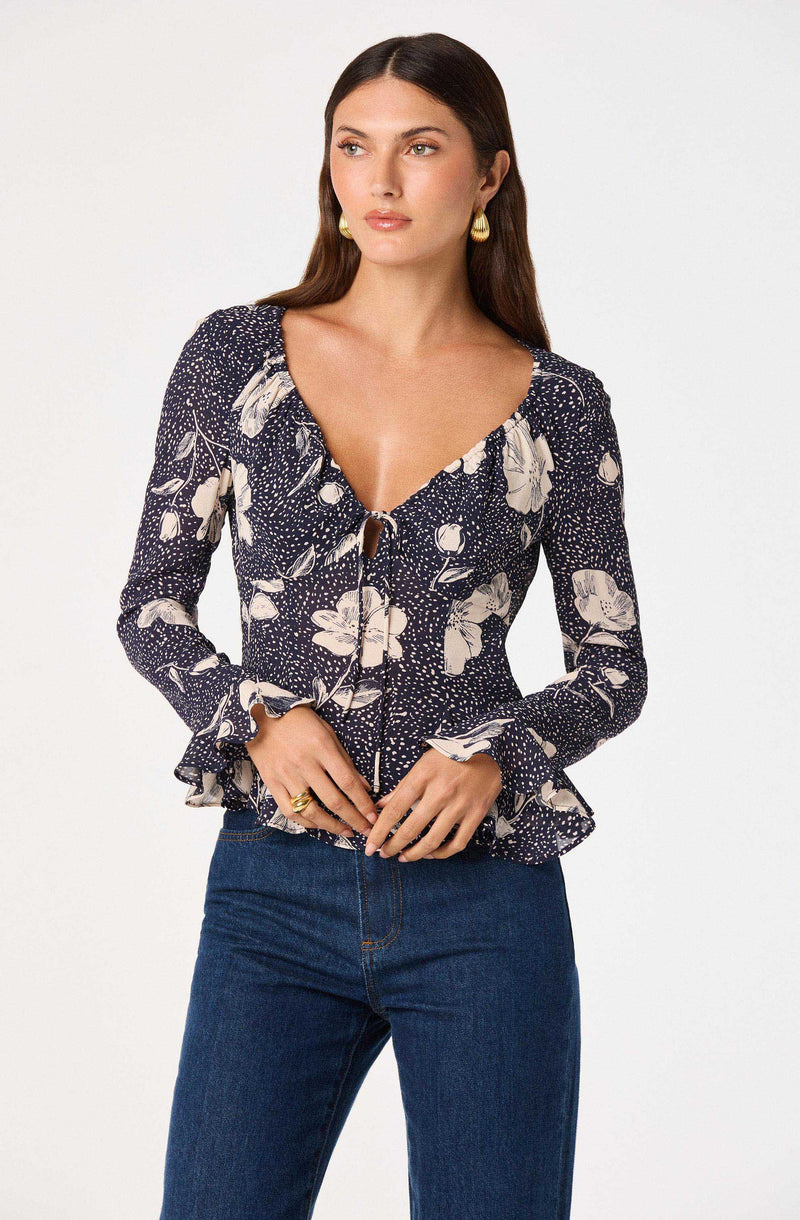 Woman wearing a navy floral print blouse with ruffled cuffs and a keyhole neckline.
