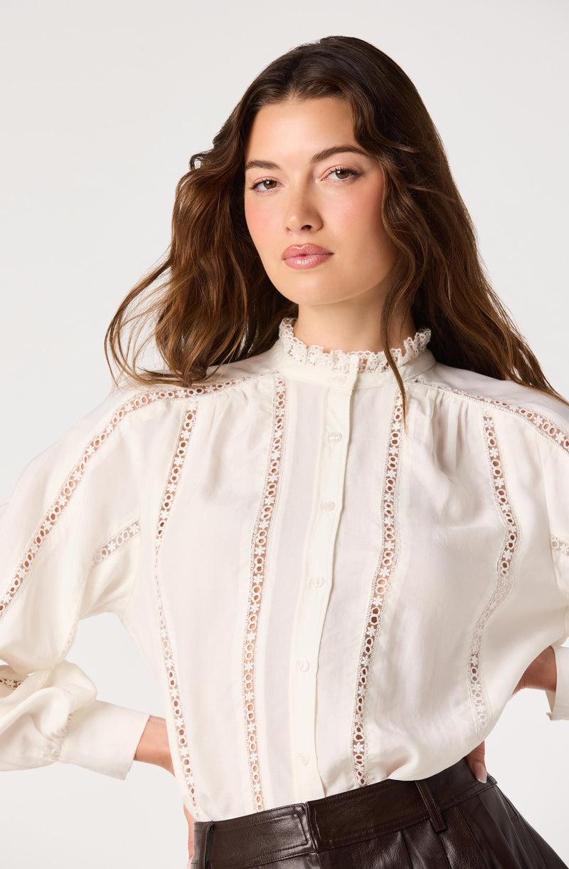 Woman wearing a cream-colored blouse with lace and eyelet details, high ruffled collar.