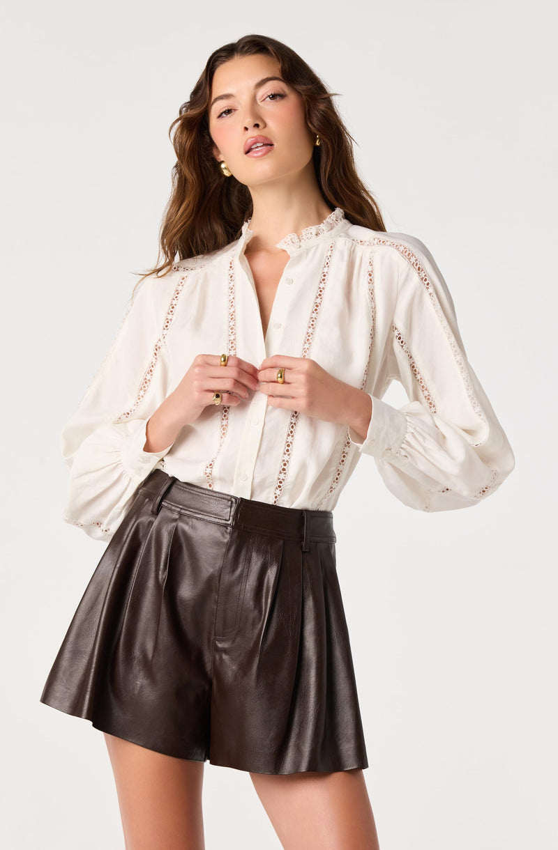 Woman wearing a white blouse with lace detail and brown leather high-waisted shorts.