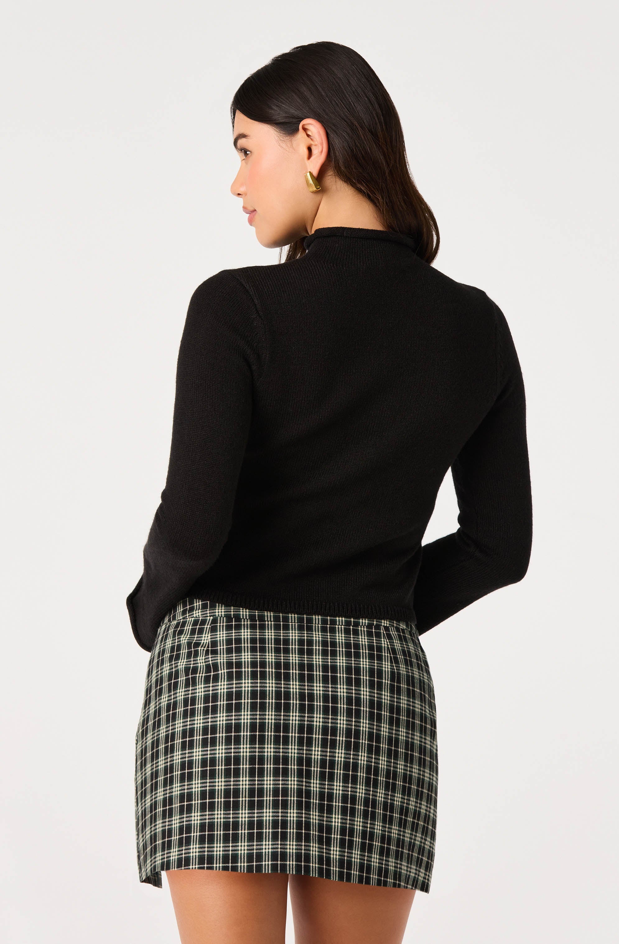 Woman wearing a black long-sleeve top and a plaid skirt.