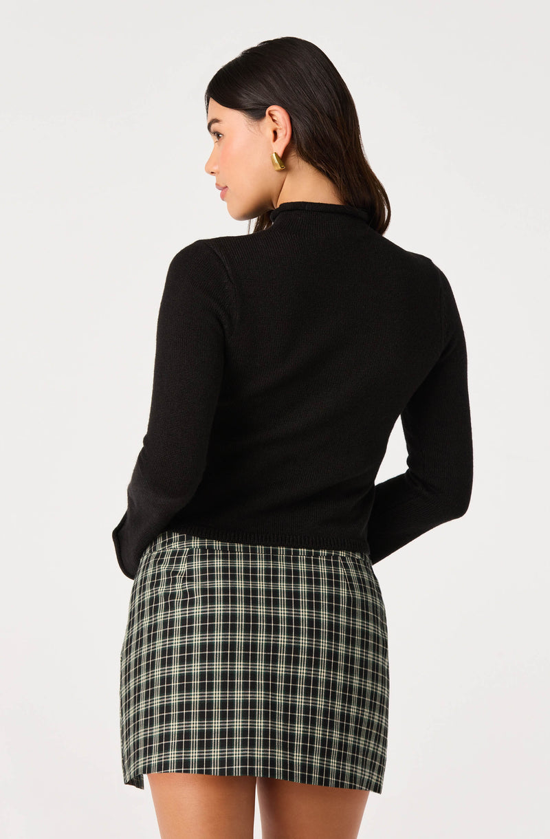 Woman wearing a black long-sleeve top and a plaid skirt.