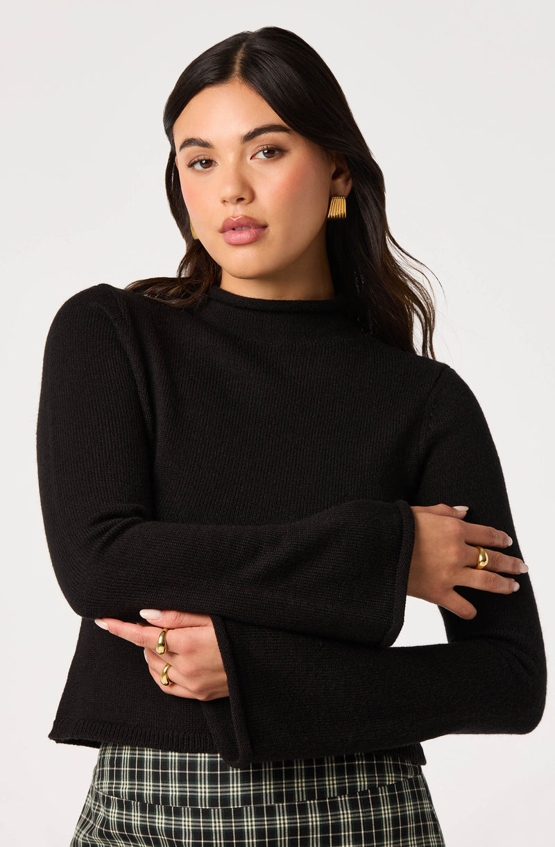 Woman wearing a black long-sleeve sweater with bell sleeves and plaid skirt.