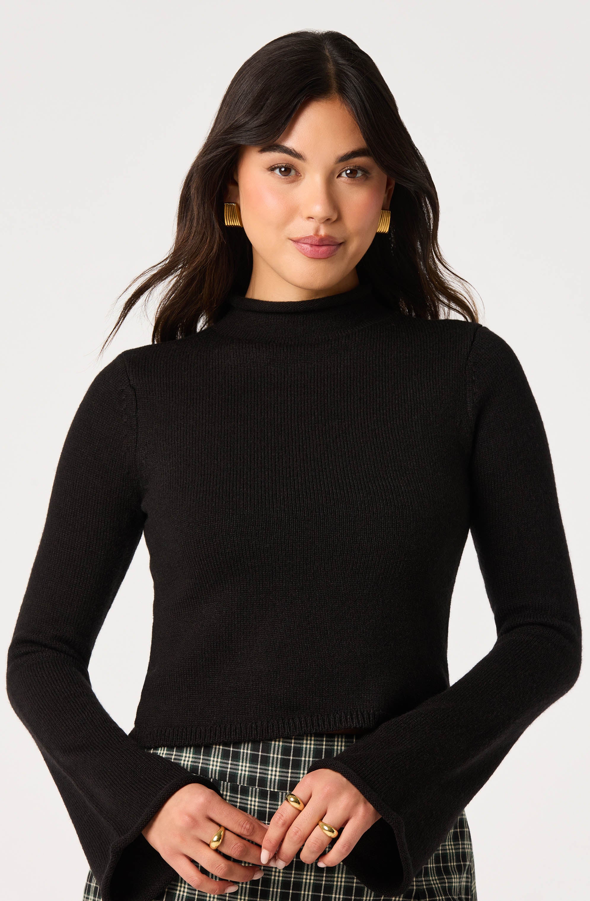 Woman wearing a black long-sleeve ribbed sweater with bell sleeves and high neckline.
