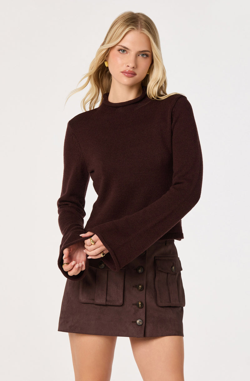 Woman wearing a dark brown long-sleeve sweater and a brown button-front skirt with large pockets.