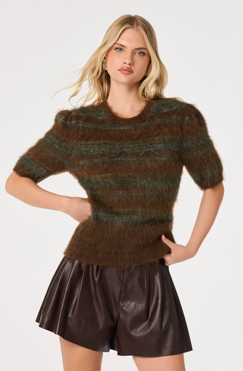 Model wearing a fuzzy, striped brown and green short-sleeve sweater and dark brown leather shorts.