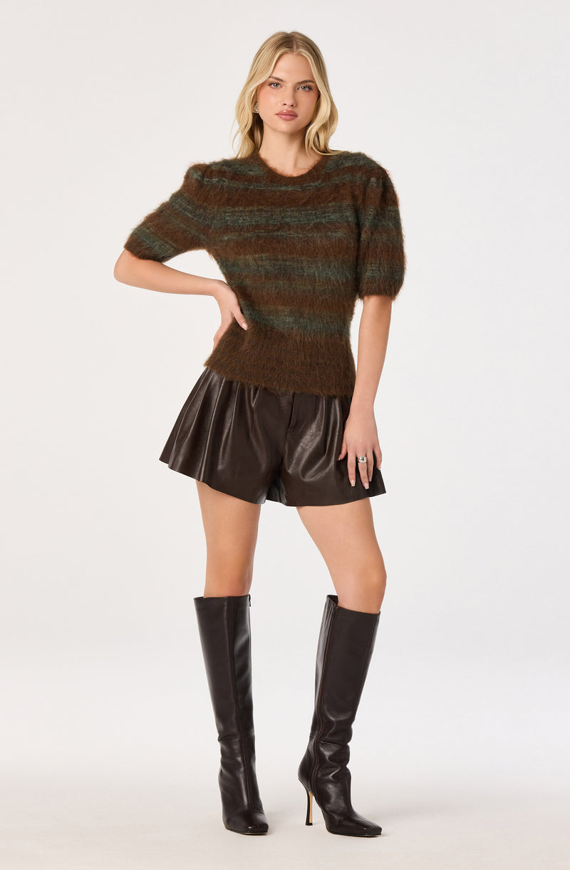 Woman wearing a multicolored knit sweater, dark leather shorts, and tall black knee-high boots.