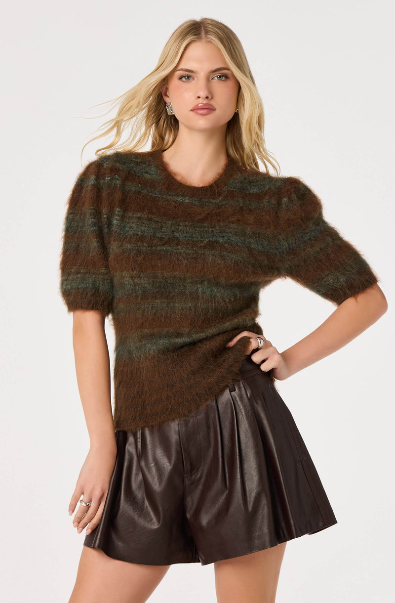 Model wearing a fuzzy, striped brown and green sweater with puffed sleeves and dark leather shorts.