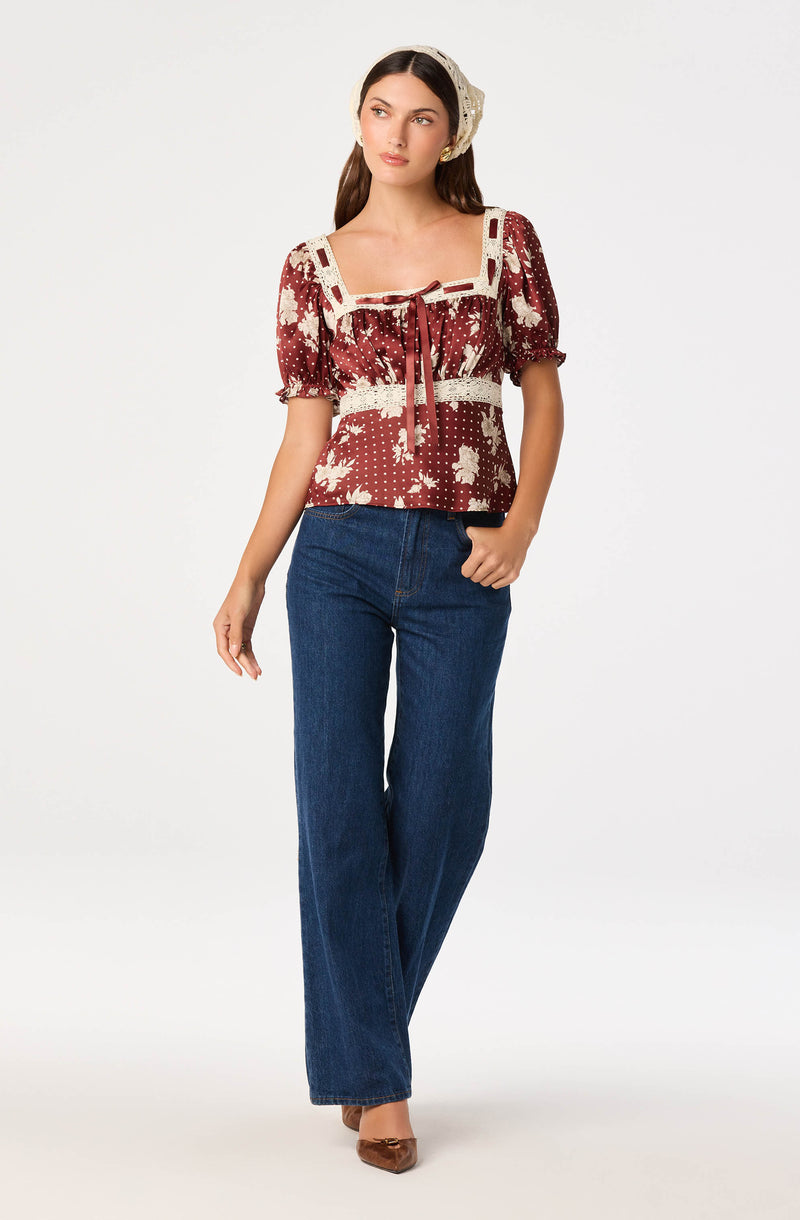 Woman wearing a red and white patterned top with lace details and puffed sleeves, paired with high-waisted blue jeans.