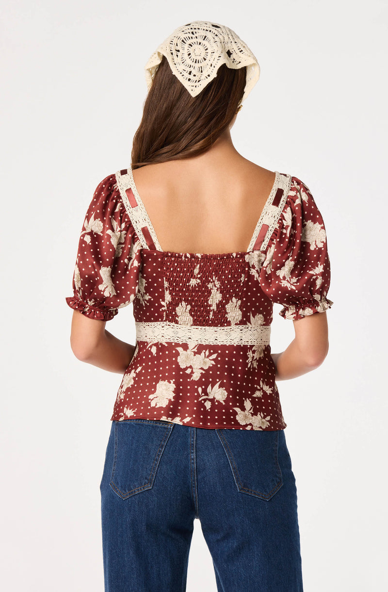 Woman wearing a brown floral top with puff sleeves and crochet details, paired with blue jeans.