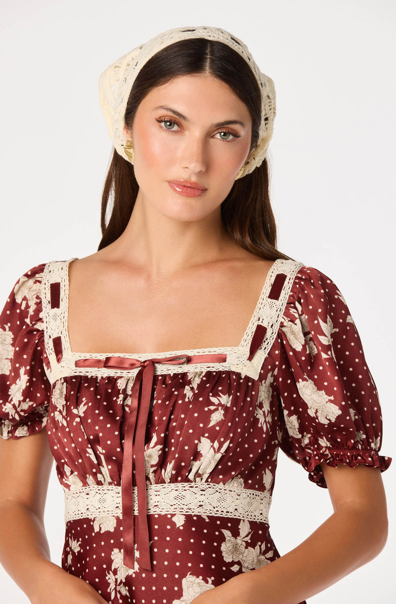 Woman wearing a vintage-style dress with a square neckline, puffed sleeves, polka dots, floral patterns, lace trim, and a ribbon tie.