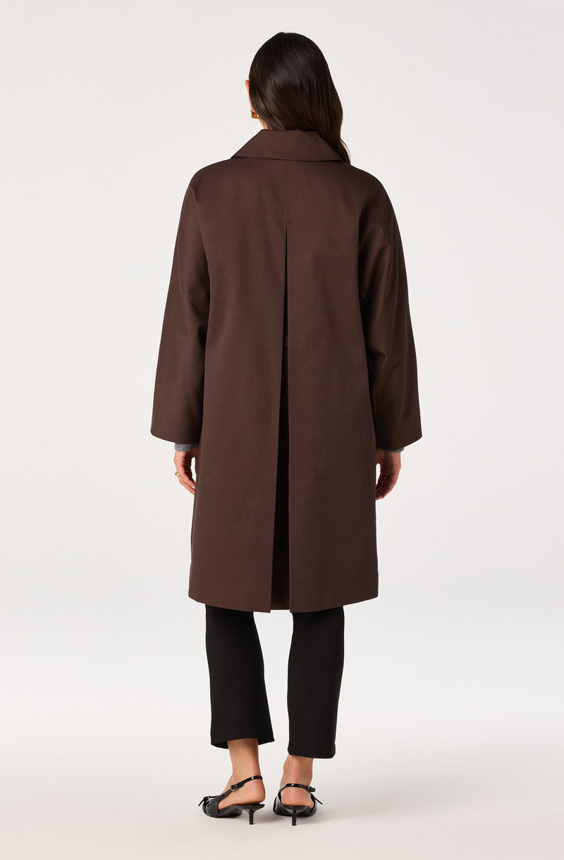 Woman wearing a long brown coat and black pants, with black strappy heels.